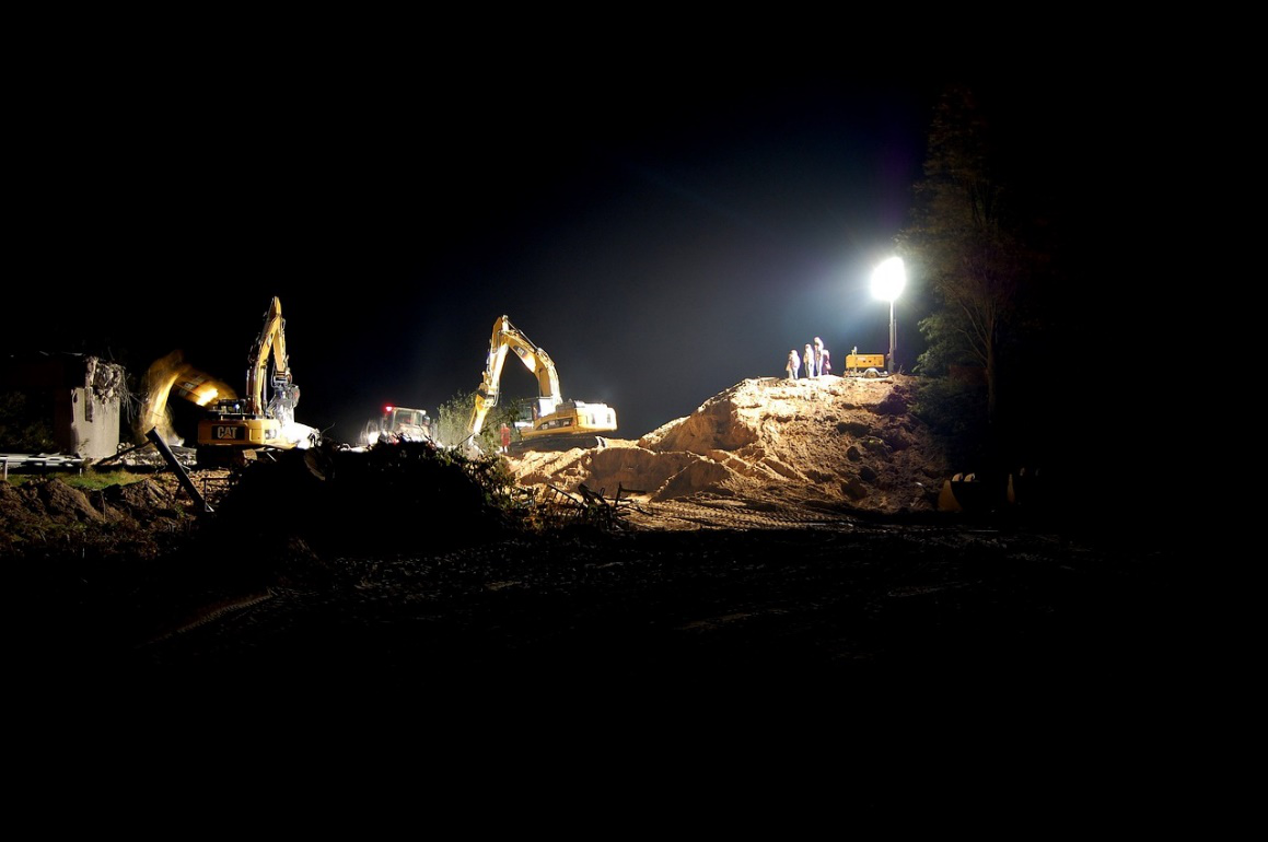 Night construction site with bright floodlights illuminating the work area.